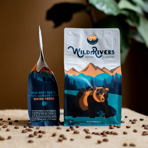 12 oz. Guatemalan DECAF coffee bag with a mountain scene and illustration of a Grizzly Bear with Wild Rivers Logo. Tasting notes for this coffee include: Milk Chocolate, Nectarine, Toffee - Decaf sticker on packaging - 6 month subscription
